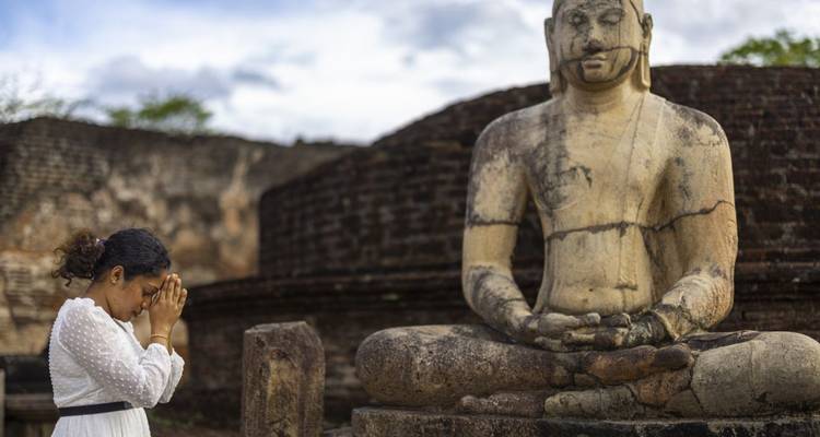 Frau, die an einem alten Tempel mit einer Buddha-Statue betet.