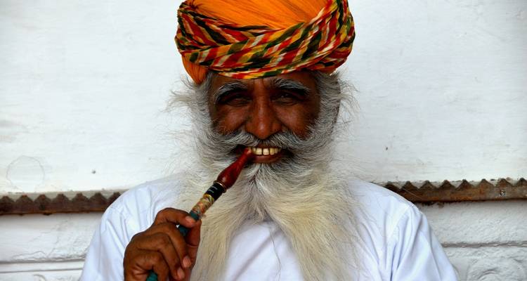 Retrato de un hombre sonriente con vestimenta tradicional sosteniendo una pipa.