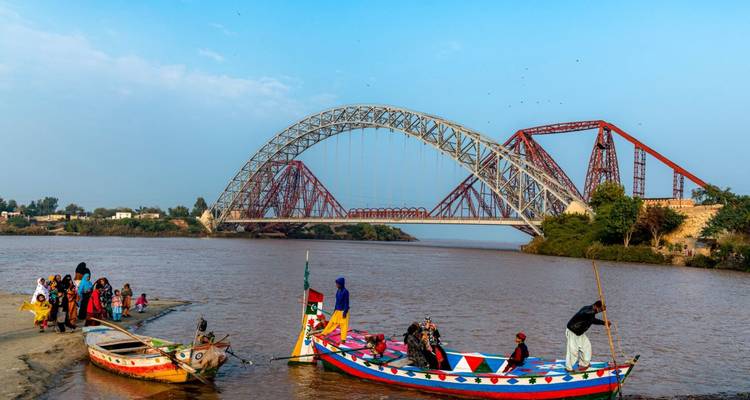 Kleurrijke boten aangemeerd bij een grote boogbrug over een rivier.