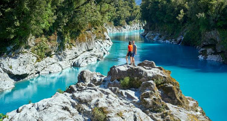 Deux personnes se tiennent sur des rochers en regardant dans une gorge de rivière d'un bleu vibrant.