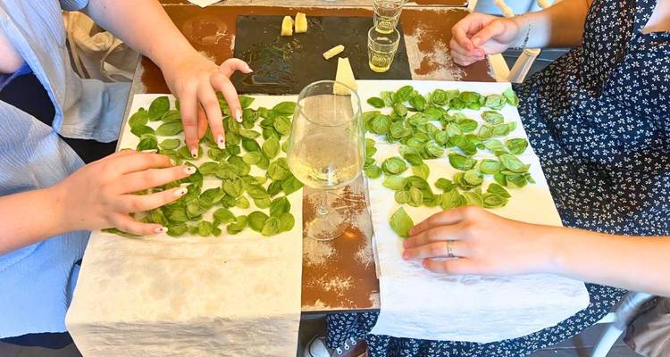 Mensen die basilicumblaadjes schikken, glas witte wijn op tafel.