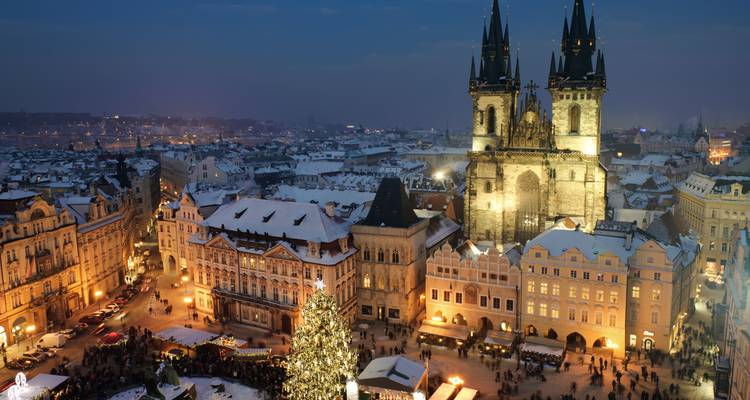 Escena nocturna de invierno de Praga con edificios iluminados y un árbol de Navidad.