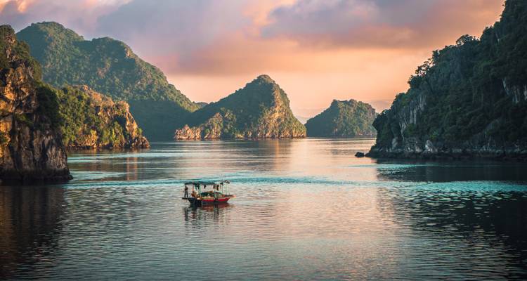 Adembenemend zonsopgangzicht van Halong Bay met boten en kalksteenformaties.