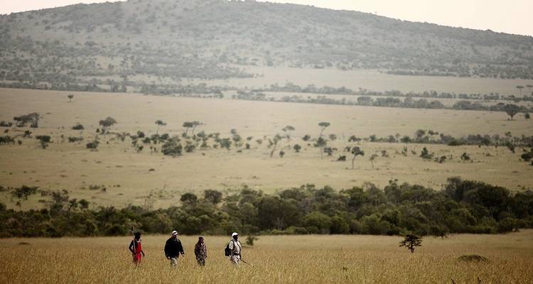 Menschen, die in einer weiten Savannenlandschaft mit fernen Hügeln wandeln.