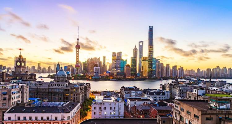 Panoramablick auf Shanghais moderne Skyline über den Huangpu-Fluss, eingerahmt von einem farbenfrohen Himmel bei Sonnenaufgang.