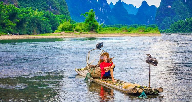 Traditioneller Fischer auf einem Bambusfloss mit Kormoranen vor der Karstkulisse des Li River.