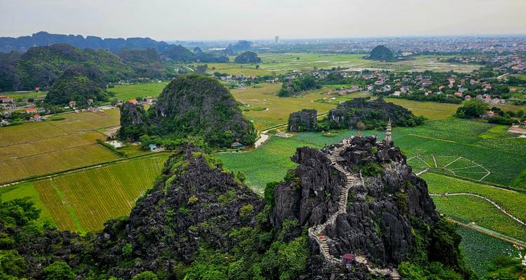 Een luchtfoto van rotsachtige heuvels en groene velden met een dorp op de achtergrond.