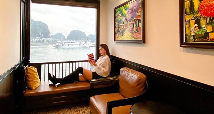 Frau liest auf einem Fensterplatz in einer Kreuzfahrt-Lounge mit sichtbaren Kalksteinkarsten draußen