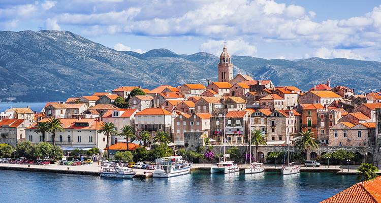 Another view of Korčula’s stone harbourfront with palm trees, historic tower and shimmering blue sea.