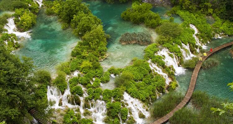 Turquoise cascades and wooden boardwalk weaving through lush greenery of a lake-filled canyon.