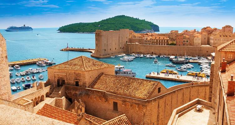 Vista soleada del puerto antiguo de Dubrovnik, fortaleza y barcos anclados con un crucero en el mar.