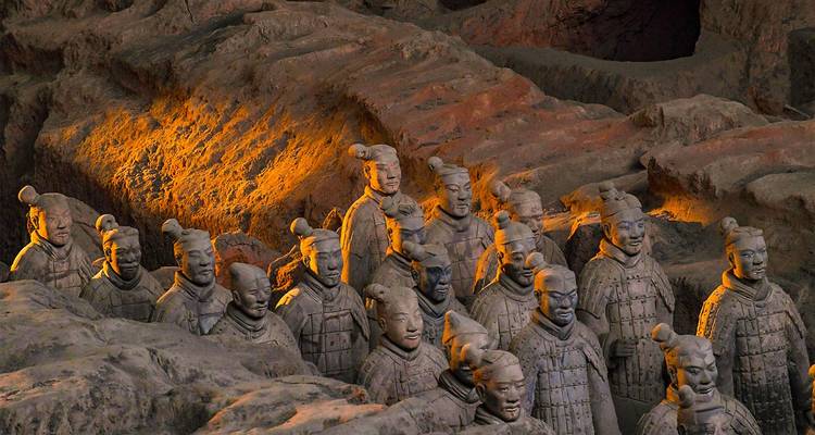 Vue rapprochée des statues de guerriers en terre cuite illuminées par une lumière chaleureuse à l'intérieur de la fosse de fouille