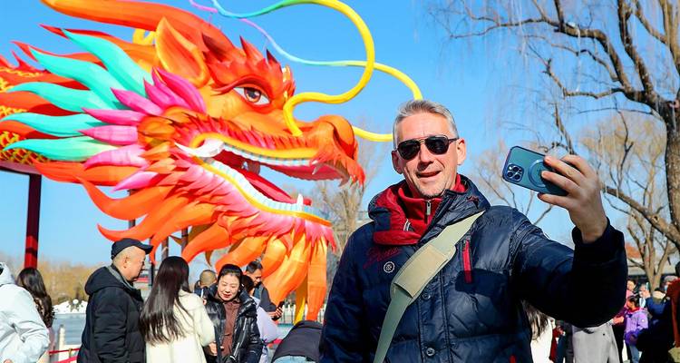 Un voyageur prend un selfie devant une immense lanterne-dragon colorée entourée de foules de festival