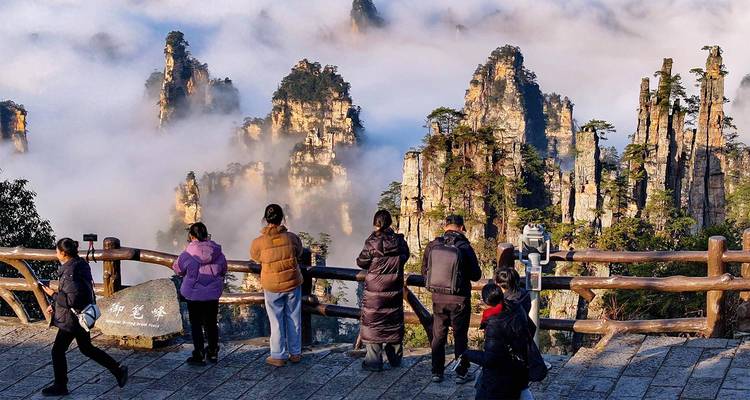 Les voyageurs s'alignent le long d'une balustrade en bois au-dessus des piliers de Zhangjiajie couverts de nuages pour admirer le lever du soleil