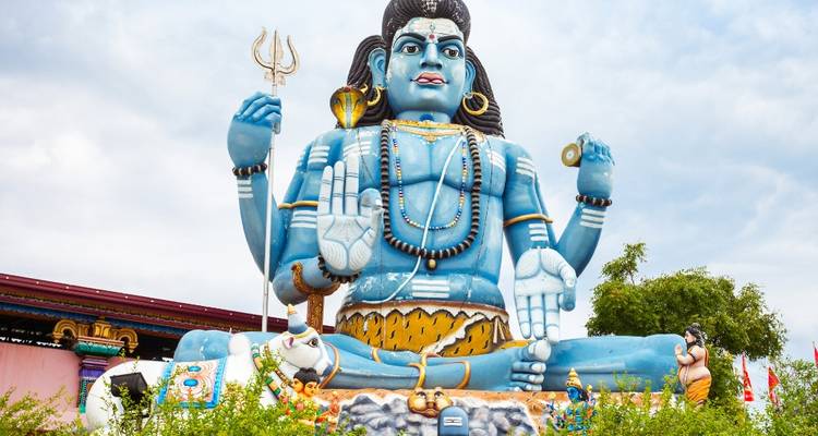 Enorm blauwe Shiva-standbeeld zittend in een open schrijn onder een bewolkte hemel