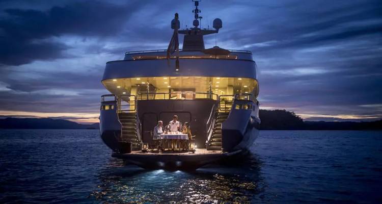 Luxusyacht-Heck bei Dämmerung beleuchtet mit elegantem Esstisch und Gästen auf ruhiger See