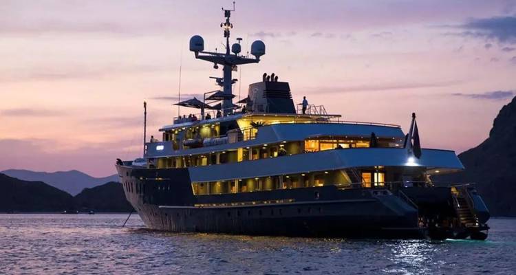 Große mehrstöckige Yacht vor Anker bei rosa Sonnenuntergang in ruhiger Bucht mit Hügeln im Hintergrund