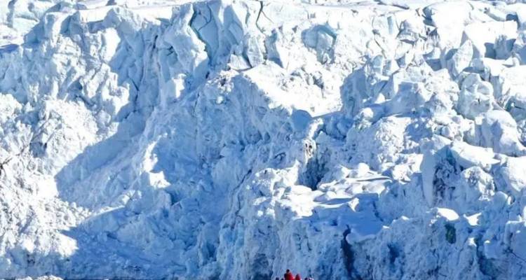Torenhoge grillige gletsjerwand met kleine roodgejaste ontdekkingsreizigers aan de voet