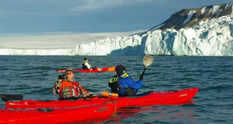 Kajakkers die peddelen langs dreigende witte gletsjerkliffen in Arctische wateren