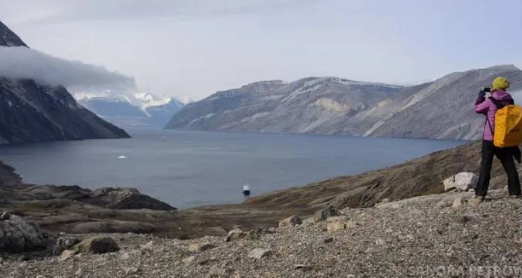 Wandelaar fotografeert brede fjord omringd door steile grijze bergen