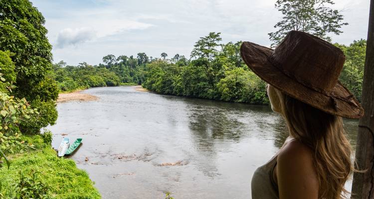 Vrouw met een hoed die uitkijkt over een rivier omringd door weelderig groen.