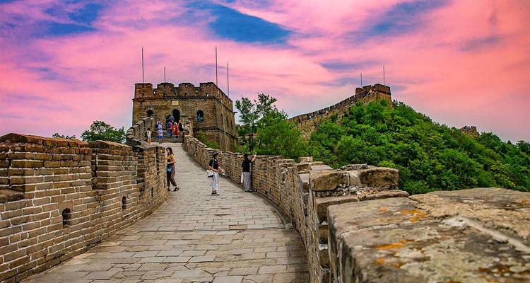 Los muros de piedra de la Gran Muralla serpentean sobre colinas verdes bajo un cielo de puesta de sol rosa vívido.