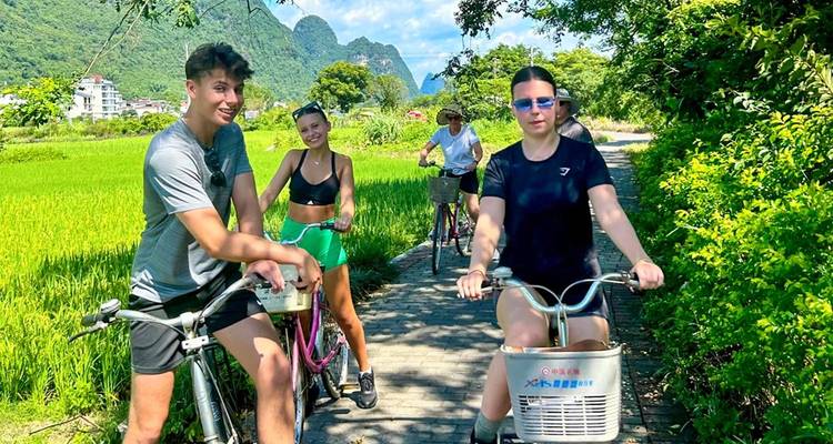 Four cyclists smile on a rural path through vivid green rice fields framed by karst peaks in Yangshuo.