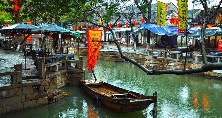 Rain-washed stone lanes and a wooden boat float through a canal town adorned with colourful banners and market stalls.