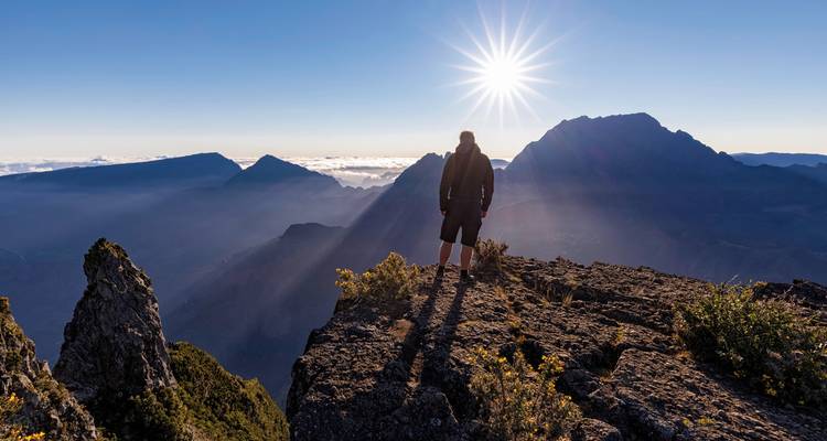Hiker standing on a mountain peak watching a sunrise.