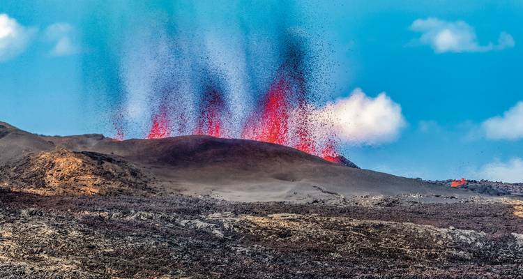 Volcanic eruption with red lava and a cloudy sky.