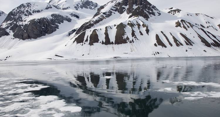 Los picos cargados de nieve se reflejan en un fiordo ártico cristalino salpicado de hielo marino flotante.
