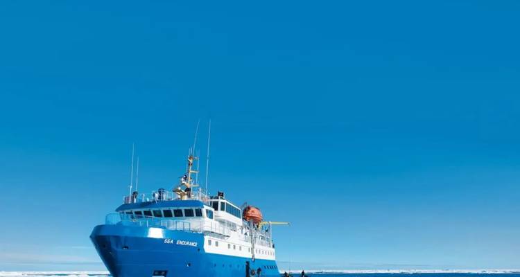 Una embarcación de expedición azul descansa sobre las tranquilas aguas del Ártico bajo un vasto cielo sin nubes.