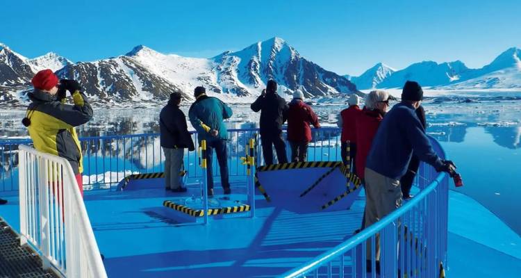Turistas envueltos en ropa de invierno fotografían montañas heladas y glaciares desde la cubierta de observación abierta de un barco.