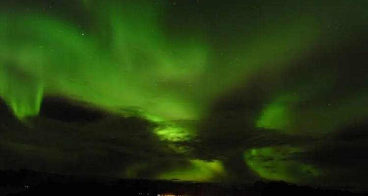 Des aurores boréales d'un vert éclatant strient un ciel arctique nocturne et sombre.