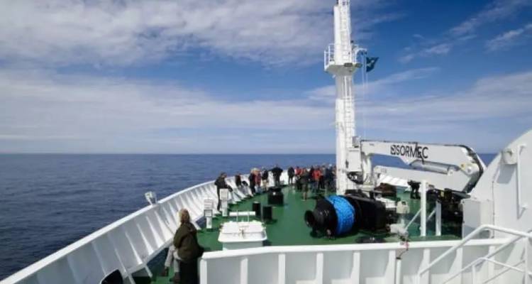 Des passagers se rassemblent sur la proue d'un navire d'expédition naviguant sur des mers calmes et ouvertes sous un ciel partiellement nuageux.