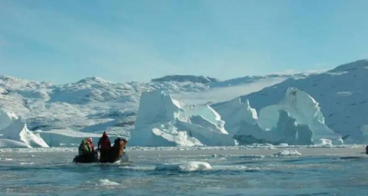 Les passagers du Zodiac approchent d'immenses icebergs bleu-blanc dans une baie glacée.