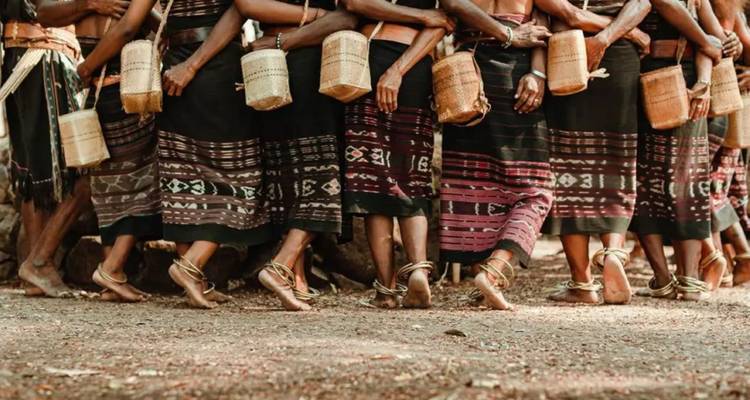 Des danseuses en jupes tissées traditionnelles se donnent le bras en exécutant une danse culturelle, de petits paniers suspendus à leurs côtés.
