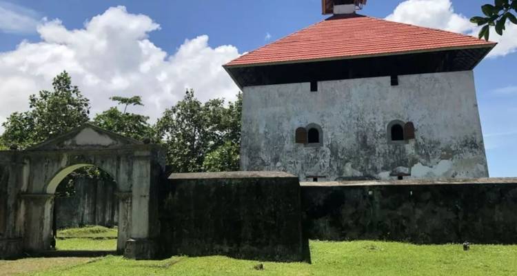 Fort historique en pierre avec un toit de tuiles rouges et une porte voûtée sur fond de ciel bleu et de pelouse verte.