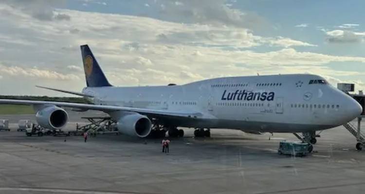 Un Boeing 747 de la Lufthansa est stationné sur une aire de trafic d'aéroport avec du personnel au sol et de l'équipement autour.