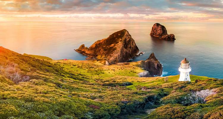 Vue panoramique côtière du phare de Cape Reinga perché au-dessus de falaises marines spectaculaires au lever du soleil