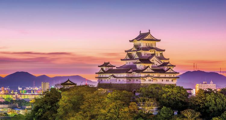 Atemberaubender Blick auf die Burg Himeji bei Sonnenuntergang mit städtischem Hintergrund.