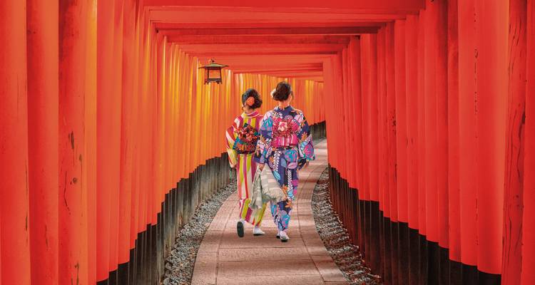 Zwei Personen in Kimonos, die durch einen traditionellen roten Torii-Tor-Pfad gehen.