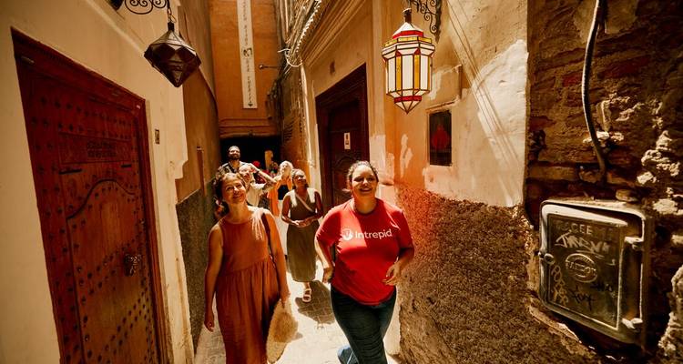 Un groupe de touristes marche dans une ruelle étroite et tachetée de soleil de la médina de Marrakech entre des murs ocre.