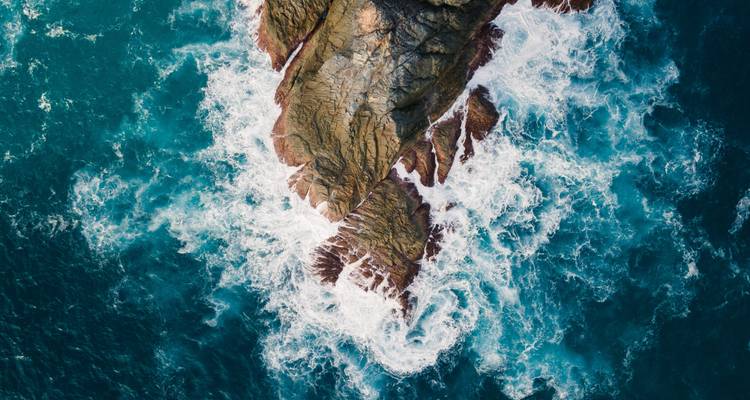 Vue aérienne de vagues qui se brisent contre des falaises rocheuses.