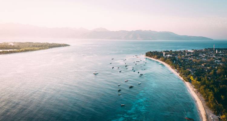 Vue aérienne d'une zone côtière avec des bateaux éparpillés et des îles au loin.