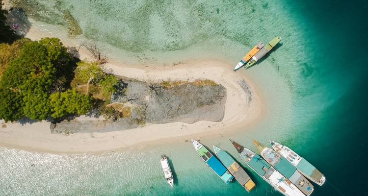 Plage de sable avec des eaux turquoise et des bateaux ancrés près d'une petite île.