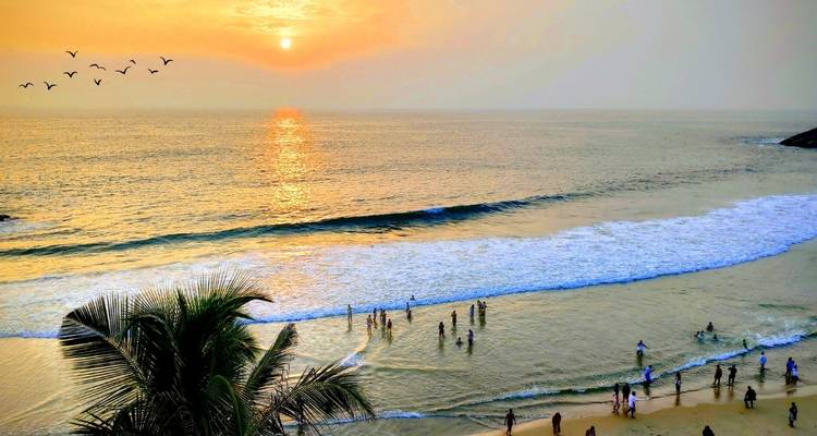 Scène de plage avec des gens qui nagent et un coucher de soleil.