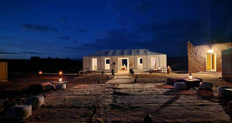 Nächtliches Wüstencamp mit beleuchteten Wegen und Zelten.