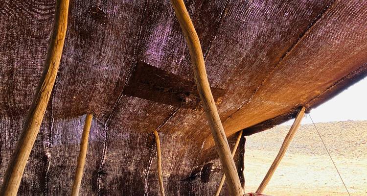 Inneres eines gewebten Zeltes mit Holzstützen in einer Wüstenumgebung.