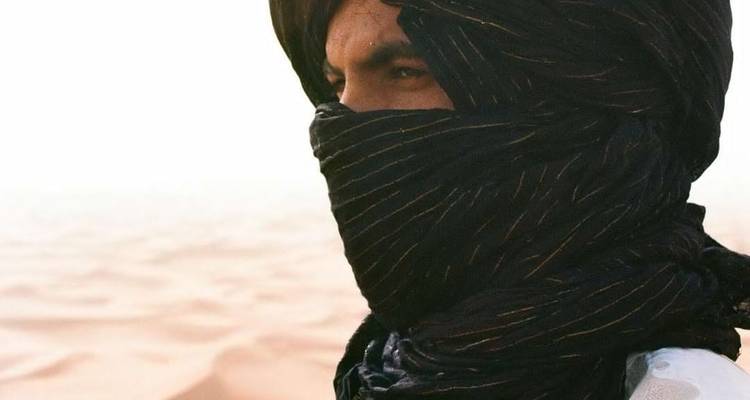 Portret van man met donkere tulband en gezichtssluier die over de woestijn staart